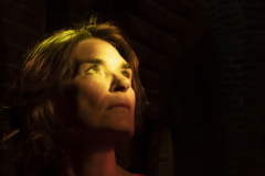 Toward the Light, Fine art portrait of a woman illuminated by dramatic golden light while looking upward into the darkness.