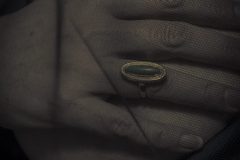 Inheritance, Fine art close-up photograph of a hand resting on a woman's chest beneath a delicate black veil, wearing a vintage green gemstone ring.