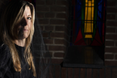 Veiled Light,Fine art portrait of a woman wearing a black veil beside a stained glass window, illuminated by dramatic light.