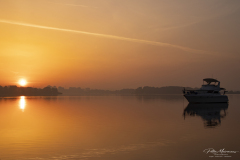 Daybreak, Fine art landscape photograph of a boat resting on calm water at sunrise beneath a golden sky.