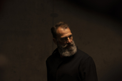 Portrait Man with beard standing in low light, looking to the side, partially illuminated against a dark